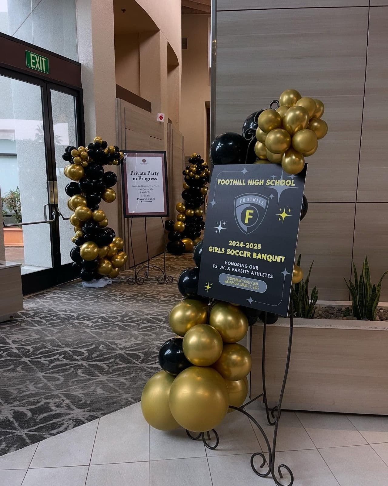 Black and gold balloon columns framing an easel sign at a high school banquet