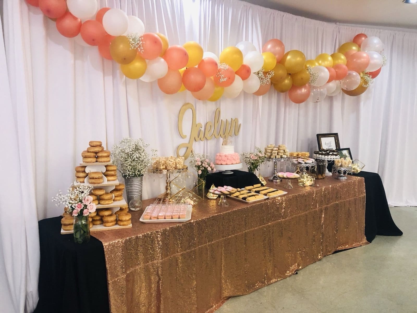 Coral, gold and white balloon garland above a sequined dessert table with a draped backdrop