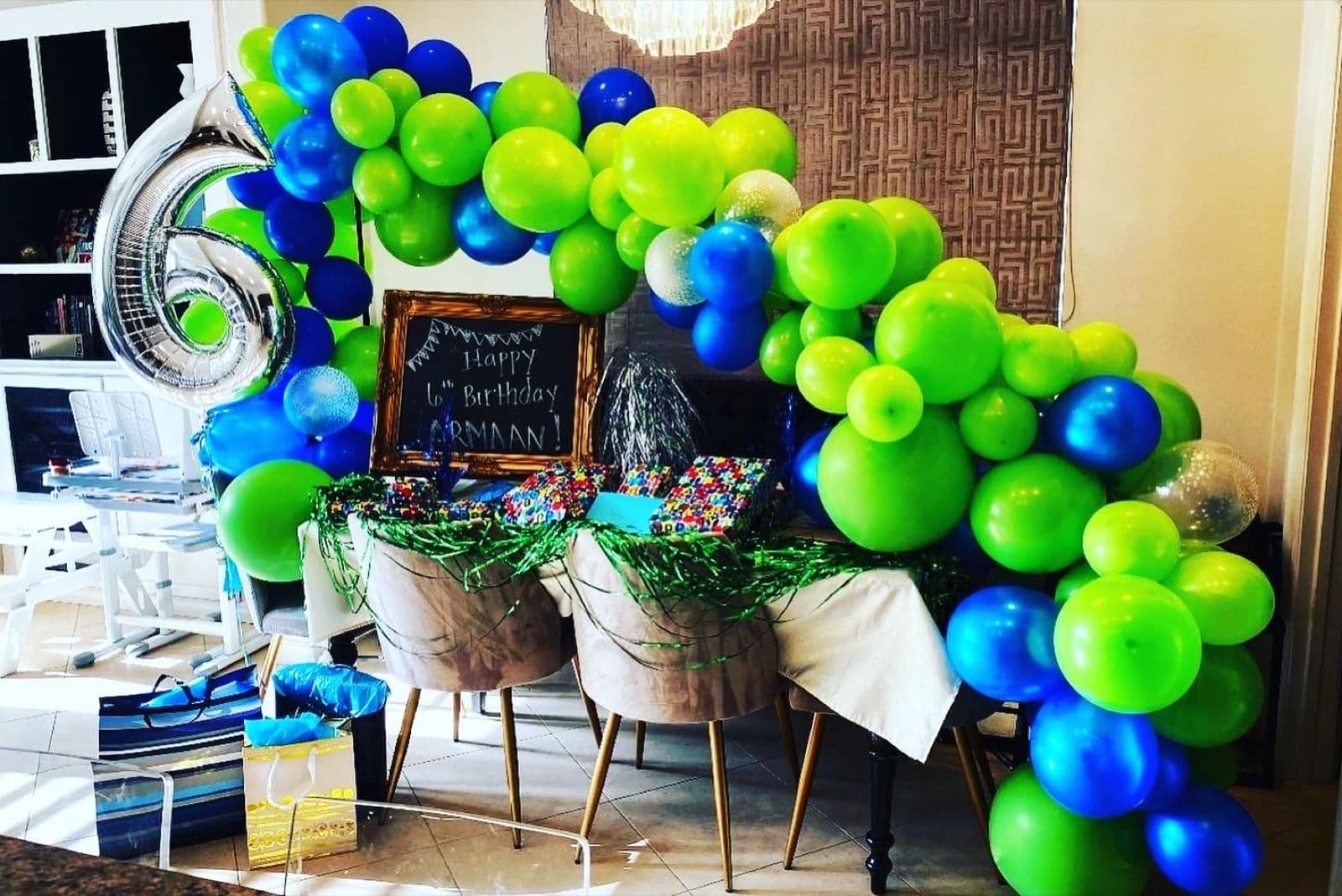 Green and blue balloon garland arching over a birthday dessert table