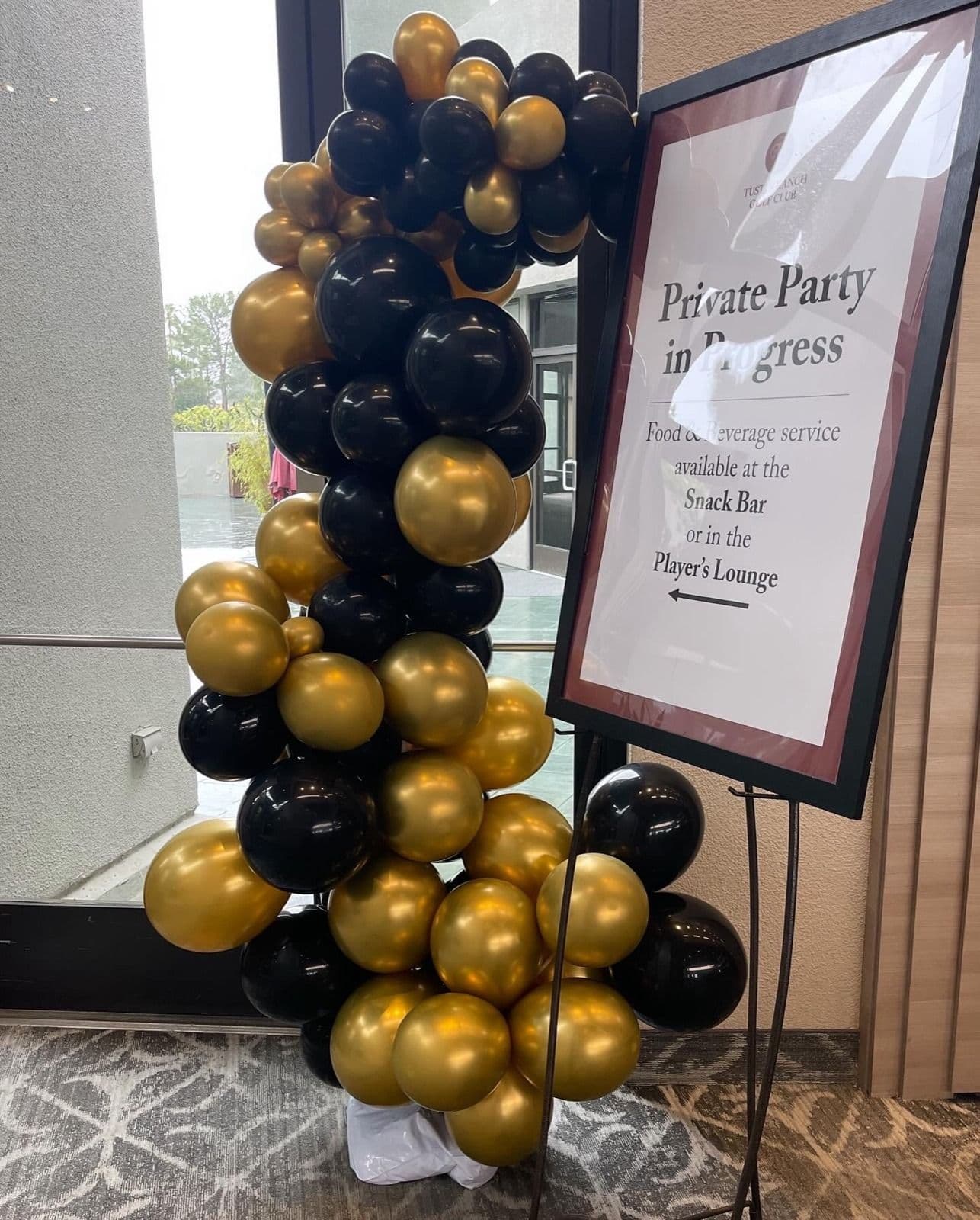 Black and gold balloon column beside a printed event sign at a venue entrance