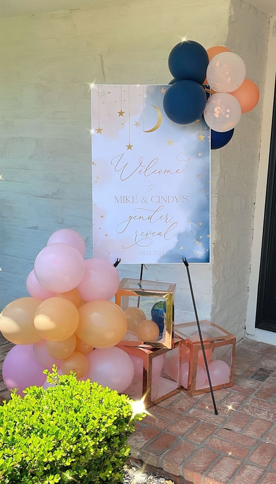 Navy, peach and blush balloon clusters around a gender reveal welcome sign