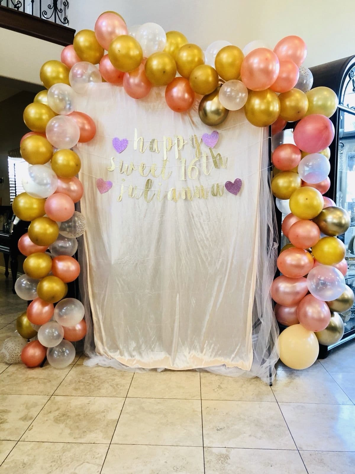 Gold and rose gold balloon arch framing a draped fabric backdrop