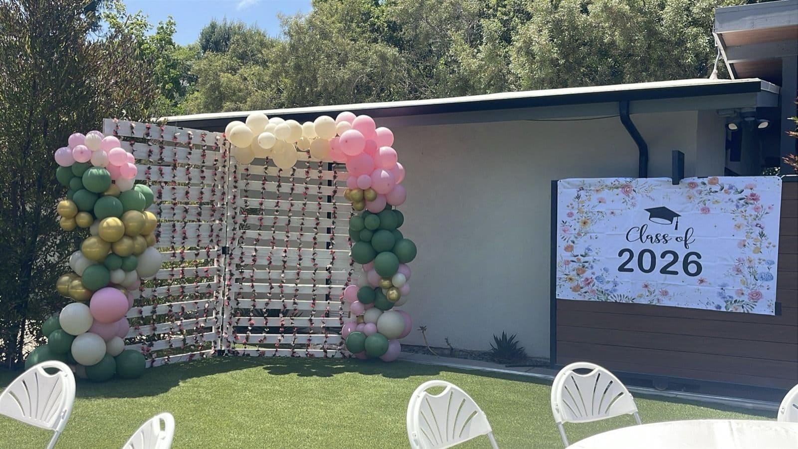 Sage, blush and cream balloon garland framing a greenery wall at an outdoor graduation party