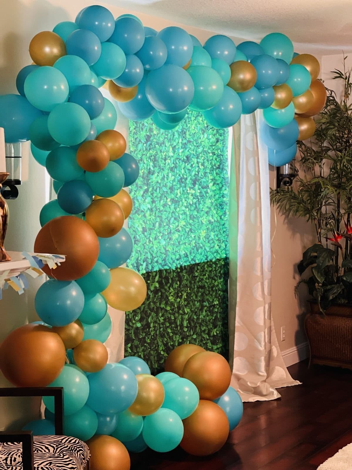 Teal and copper balloon garland framing a greenery wall backdrop