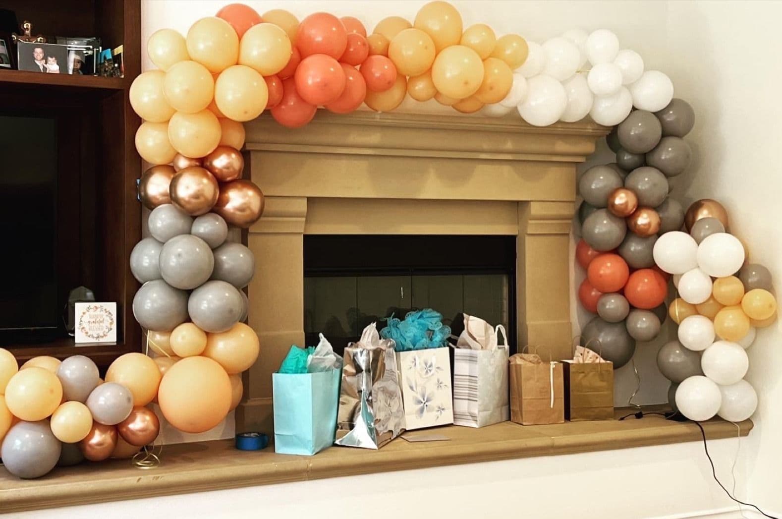 Peach, copper and grey balloon garland wrapped around a stone fireplace mantel above a gift table