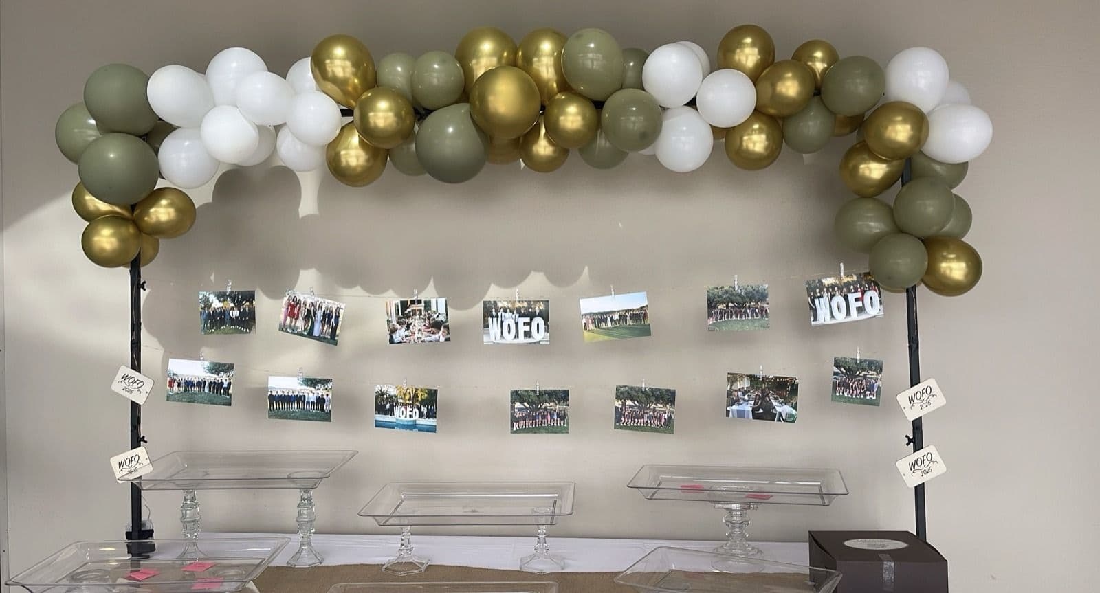 Sage green, gold and white balloon garland above a wall of framed photographs