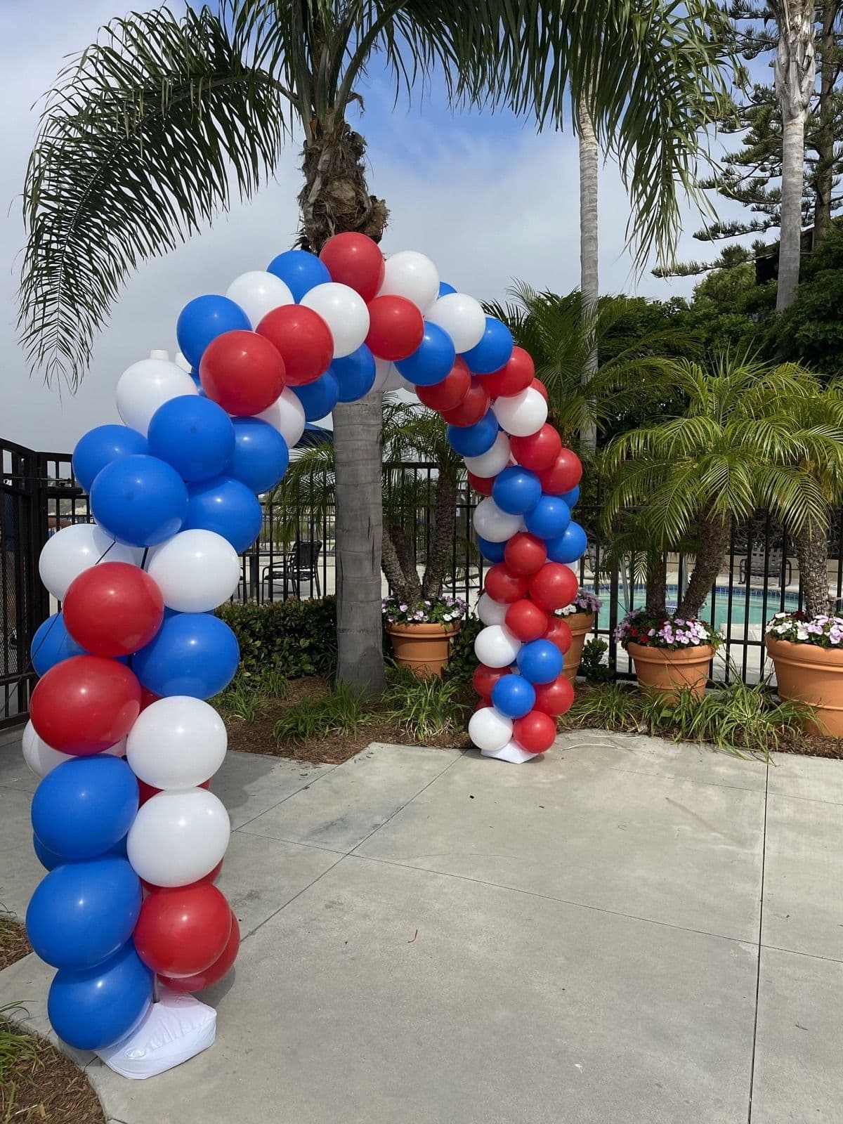 Red, white and blue balloon arch beside a palm-lined pool