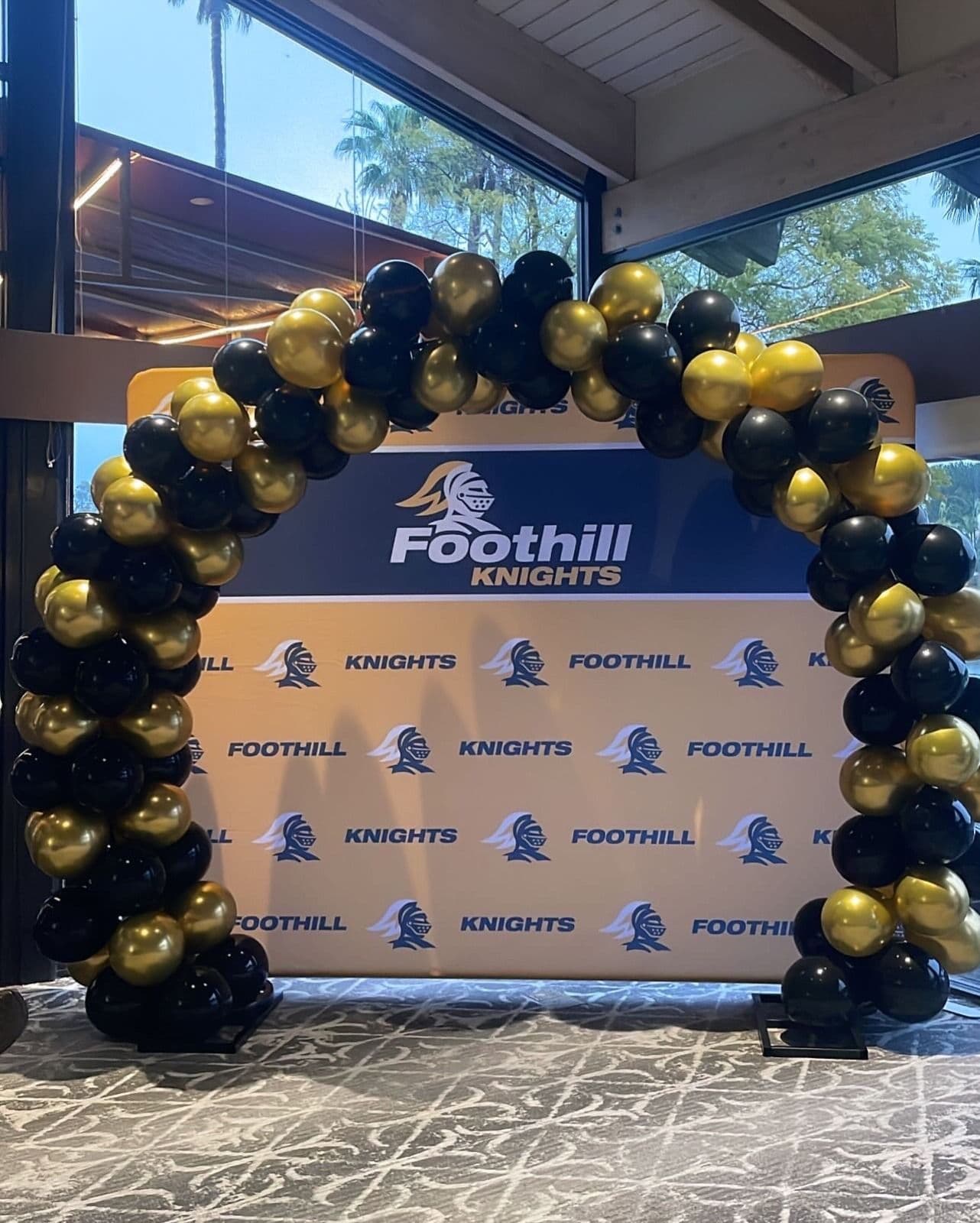 Black and gold balloon arch over a school step-and-repeat banner