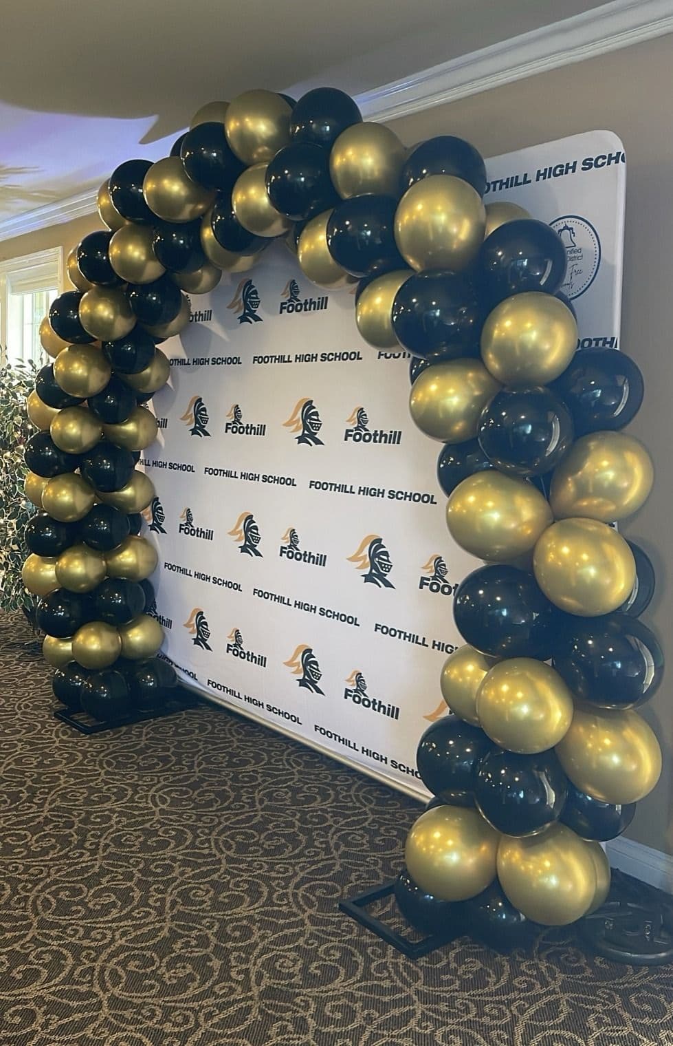 Navy and gold balloon arch over a school step-and-repeat backdrop