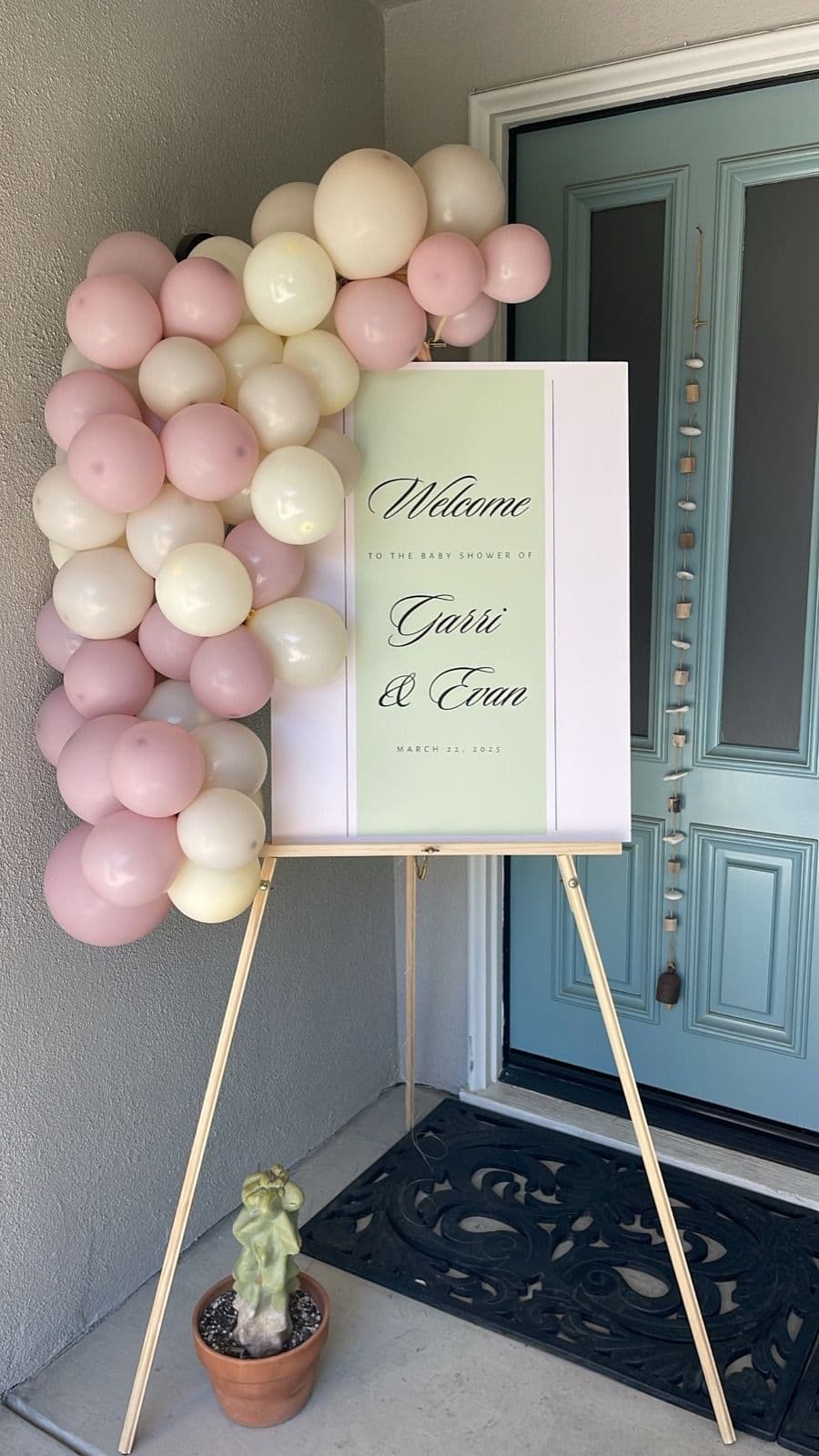 Blush and cream balloon cluster on a welcome sign easel beside a front door