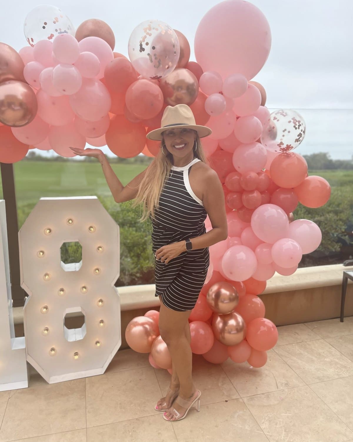 Vanessa Chaverst, Founder & CEO of Events by Ness, beside a blush and rose-gold balloon garland and a lit marquee number